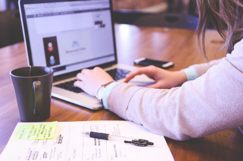 Person researching information at a computer with a coffee mug, notepad, and pen next to them on the desk.